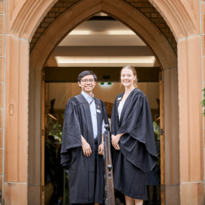 Two students stand in academic gowns at our main entrance